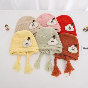 Detailed view of colorful knit baby hats featuring plush cartoon bear patches and tassels