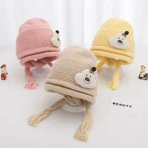 Detailed close-up of thick knitted baby hats in pink, beige, and yellow with bear patch