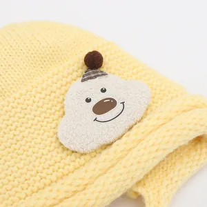 Close-up of a yellow knitted baby hat featuring a 3D cartoon bear patch with soft texture