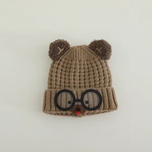 Detail of a brown knitted children's hat with bear ears and cartoon glasses decorations