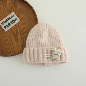 Detail of light pink knitted beanie featuring a cartoon coffee cup patch and soft texture