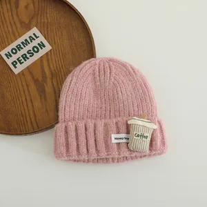 Close-up of pink knit beanie with coffee cup patch and ribbed texture detailing