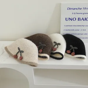 Détail de quatre bobs en maille avec décorations cerises et bordures contrastées