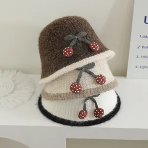 Détail de chapeaux cloches en tricot avec cerises et nœuds en marron, beige et blanc