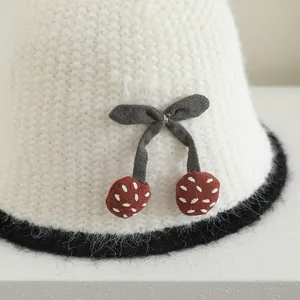 Détail du chapeau en tricot avec bord pelucheux, nœud gris et motifs cerises