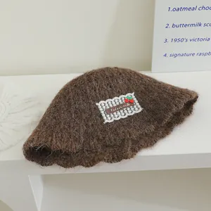 Détail d'un chapeau cloche en maille marron avec fleur en dentelle blanche et cerise