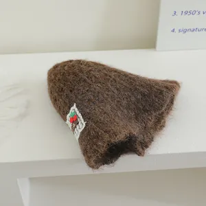 Détail d'un chapeau cloche en maille marron avec patch cerise et bordure en dentelle