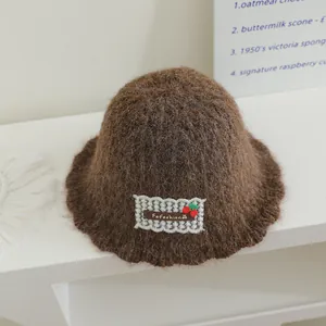 Gros plan du chapeau cloche en maille pelucheuse marron avec écusson cerise et texture douce