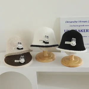 Détail de quatre bobs en tricot beige, blanc, noir et marron avec décor de lapin