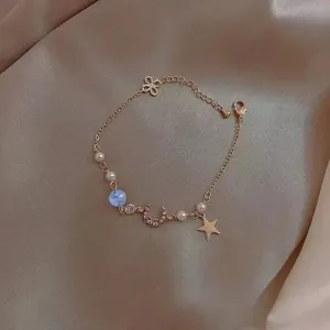Détail d'un bracelet doré avec étoile, lune, perles et nœud sur fond de soie douce