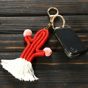 Handmade red woven cactus keychain with white tassels and pink pom poms on wood background