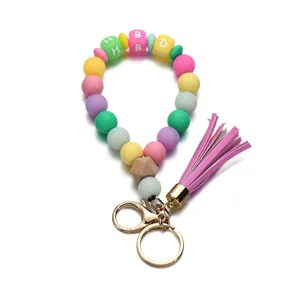 Détail de perles en silicone macaron avec lettres et pompon sur bracelet porte-clés