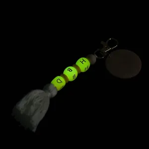 Luminous silicone bead keychain with HBD letter charms and white tassel on black backdrop