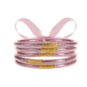 Detalle de pulseras de silicona con purpurina rosa y cierres dorados sobre cinta seda