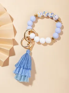 Close-up of blue floral silicone bead bracelet with golden hardware and layered fabric tassel