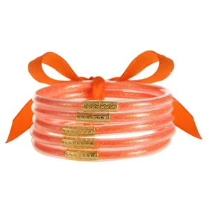 Detalle de pulseras de silicona naranja con purpurina y conectores de metal dorado