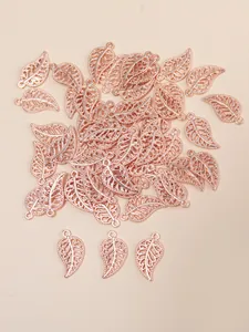 Macro shot of rose gold hollow leaf charms for DIY jewelry making on pink background