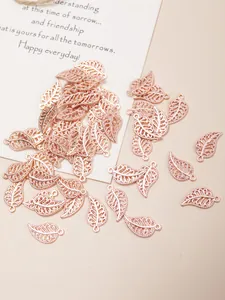 Detailed view of rose gold hollow leaf pendants and DIY jewelry charms on a beige fabric