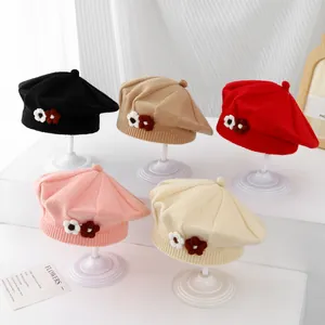 Detail view of five colors of knit beret hats for kids with floral patchwork accents