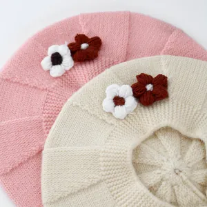 Detailed texture of knit baby berets with handmade floral accents in soft pink and beige