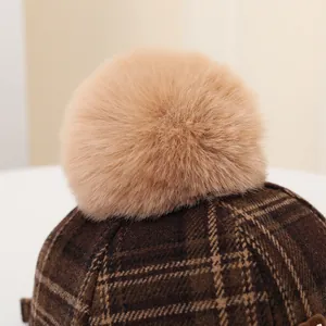 Close-up of fluffy pom-pom and vintage brown plaid texture on winter baseball cap