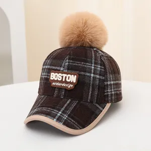 Detail of a kids plaid baseball cap featuring a large pompom and BOSTON embroidery