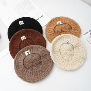 Detail of knitted baby berets in five colors with cute smiley face woven labels