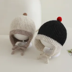 Detail van gebreide babymuts met oorkleppen, zachte textuur en decoratieve pompons