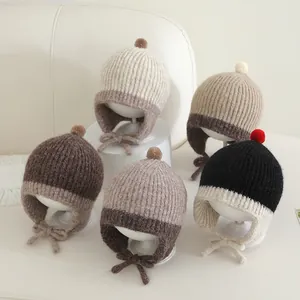 Vijf gebreide baby mutsen met pompons en oorkleppen in neutrale herfstkleuren
