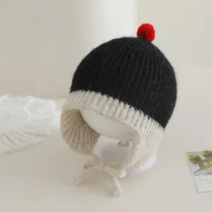 Detail van gebreide babymuts met oorkleppen, pompons en kinbandjes voor de winter