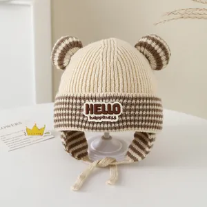 Detailed knit texture of beige winter baby hat with striped ears and HELLO embroidery