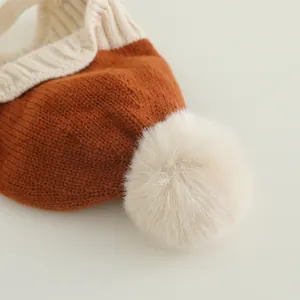 Nahaufnahme der Strickstruktur in Karamell und Creme mit Bommel auf der Baby-Wintermütze