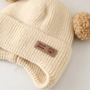 Macro detail of infant knit hat featuring a leather 'Hand Made' bear label and texture