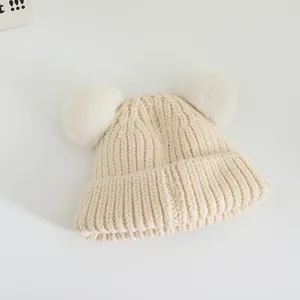 Close-up of beige knit baby hat featuring fluffy white faux fur pompom ears and textured weave