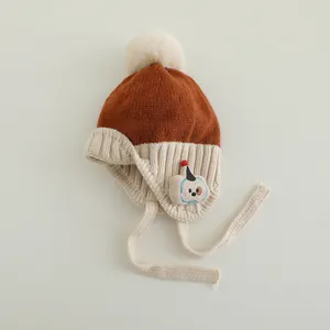 Detail der Baby-Strickmütze mit braunem Pompon und süßem Cartoon-Hunde-Aufnäher