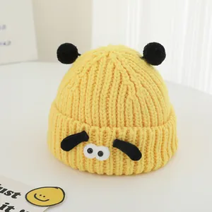 Détail d'un bonnet tricoté jaune pour enfant avec pompons noirs et oreilles de chien