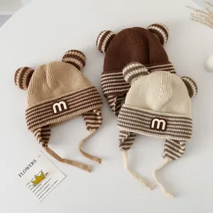 Close-up of knit baby winter hats with cute M patch, ears and straps in neutral colors