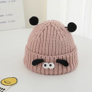 Détail du bonnet en tricot rose pour bébé avec de grands yeux et des pompons noirs