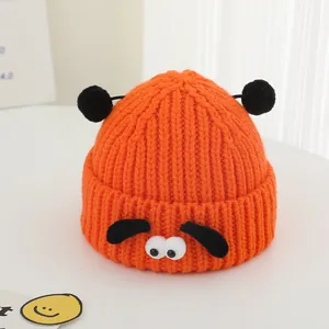 Détail du bonnet en tricot orange pour bébé avec visage de chiot et pompons noirs