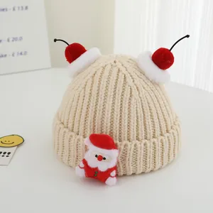 Detail of chunky knit beige Christmas hat for kids with Santa doll and red cherry pom-poms