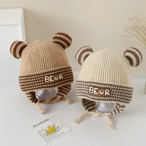 Detail showing knit baby hats with bear ears and chin straps in khaki and cream