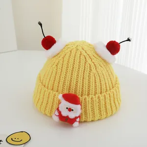 Detail of yellow knit Christmas hat with Santa patch and red pom-poms for toddlers
