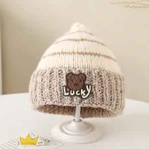 Dettaglio del berretto in maglia invernale con toppa orso e scritta Lucky beige