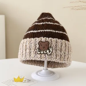 Dettaglio ravvicinato di un cappello invernale a maglia a righe con patch orsetto Lucky