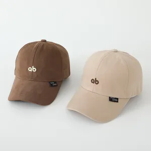 Detailweergave van twee honkbalpetten in bruin en beige met geborduurde AB-letters