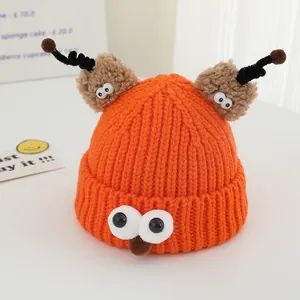 Close-up of bright orange monster knit hat with plush antennas and cartoon eye details