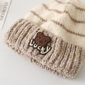 Dettaglio della toppa dell'orso Lucky su un cappello di maglia a righe beige e marrone