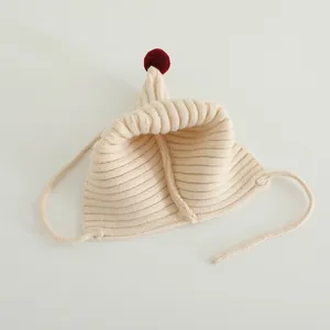 Detailed knit texture of a cream pointed baby elf hat with a red pompom and side ties