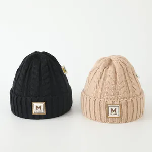Détail du tricot torsadé épais et du patch en cuir lettre M sur ces bonnets d'hiver