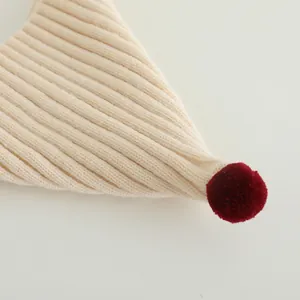 Detail of ribbed knit baby hat in beige with a decorative red plush pom-pom